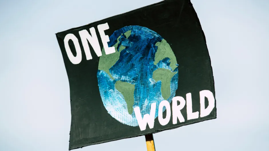 Ein Schild mit dem Ausdruck "One World" wird hochgehalten.